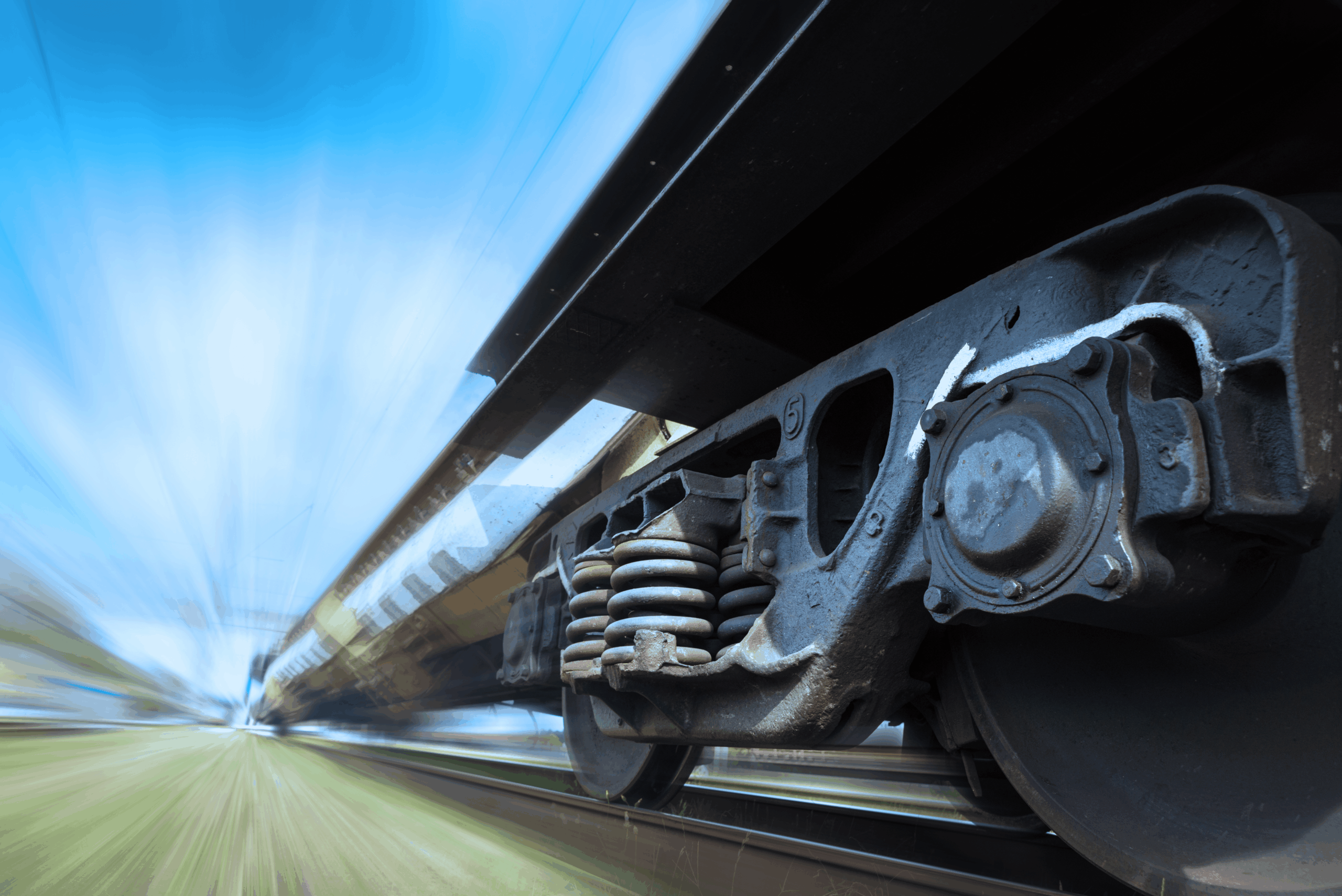 Close-up of a moving train wheel and suspension system with a blurred background, suggesting high speed.
