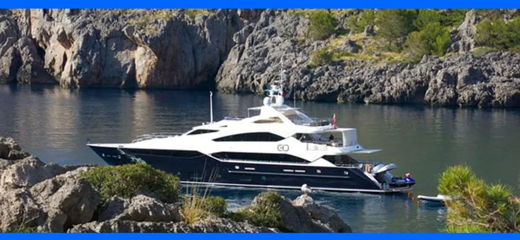 Luxury yacht anchored in a calm bay surrounded by rocky cliffs and greenery.