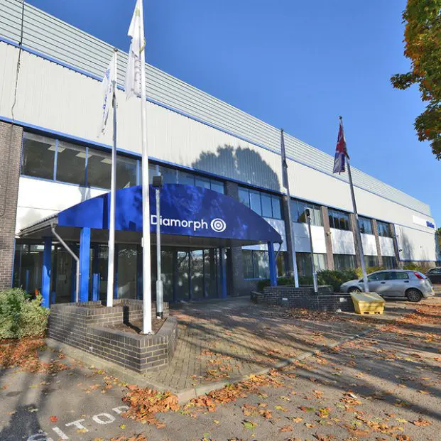 A modern office building with a blue Diamorph canopy and three flagpoles at the entrance.