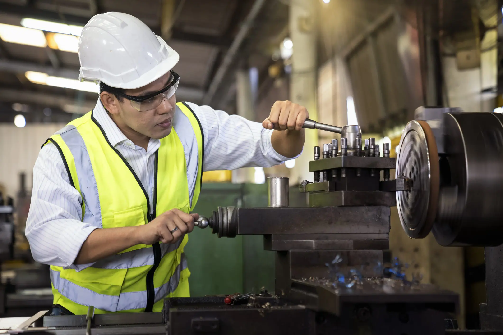 Man in safety gear operates a lathe machine in an industrial workshop.