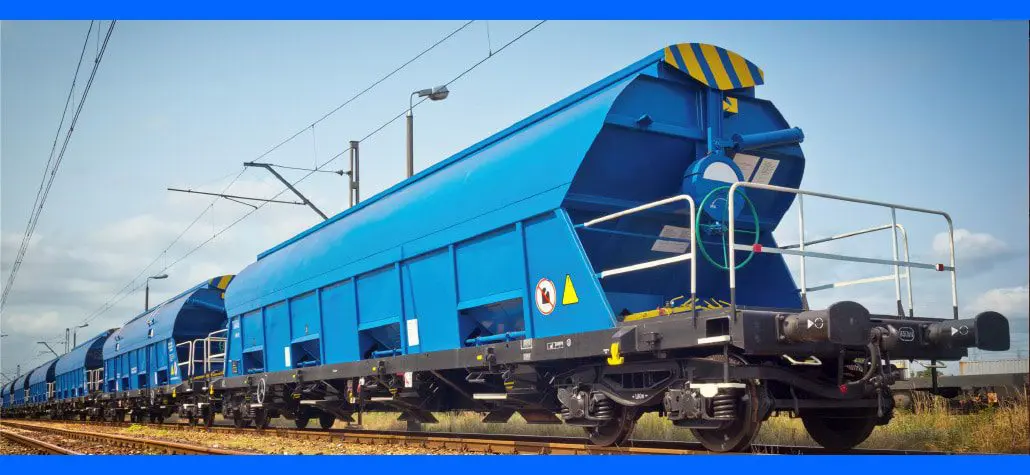 Bright blue freight train cars on railway tracks under a partly cloudy sky, viewed from a low angle.