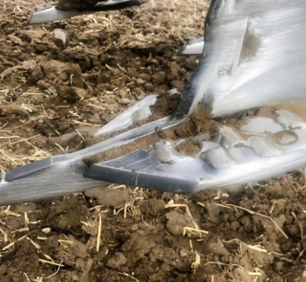 Close-up of a metal plow blade with soil stuck to it, resting on tilled earth.