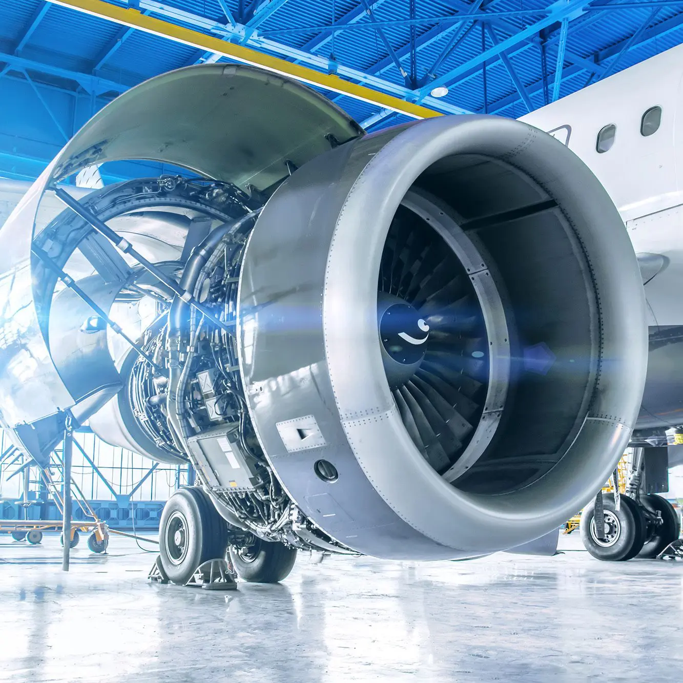 Close-up of a jet engine attached to an aircraft inside a brightly lit hangar.