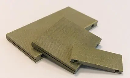 Three rectangular greenish-grey composite plates stacked on a white surface, each with a hole near one edge.