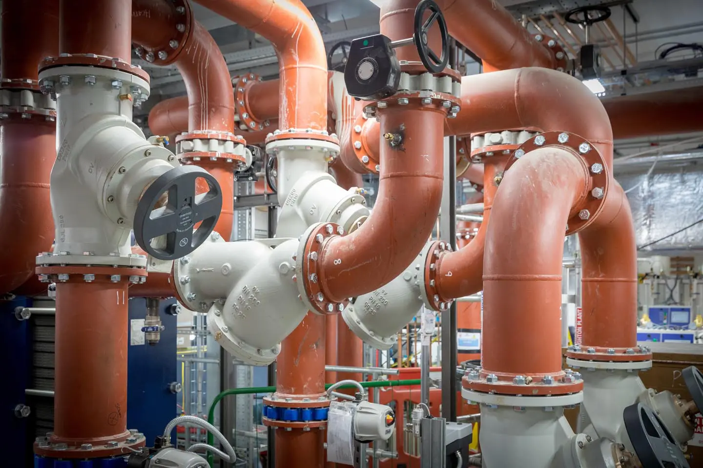 Large red and white industrial pipes and valves in a mechanical room or facility.