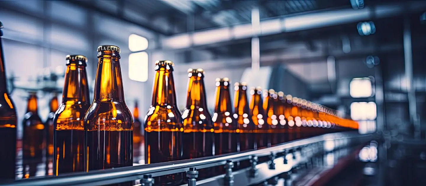 Rows of brown glass bottles on a conveyor belt in a modern beverage factory.
