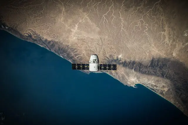 A satellite orbits above a coastal landscape, showing land and ocean from space.