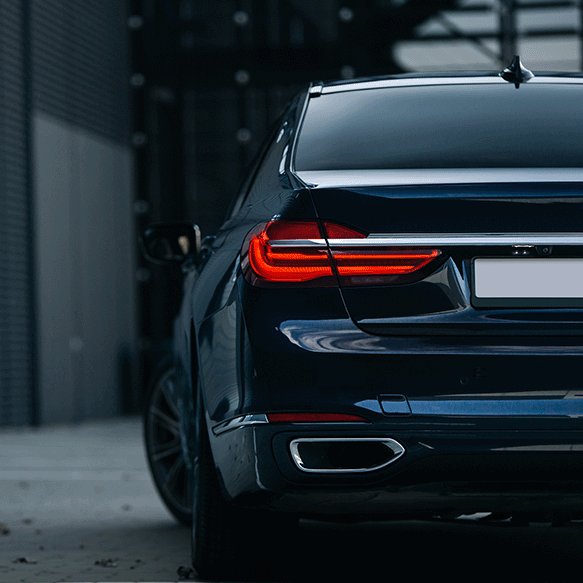 Rear view of a dark blue luxury sedan with red tail lights illuminated, parked in an urban setting.