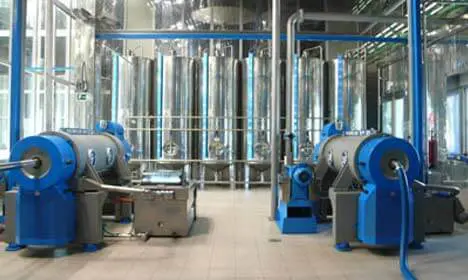 Industrial facility with large blue machinery and multiple tall stainless steel tanks in the background.