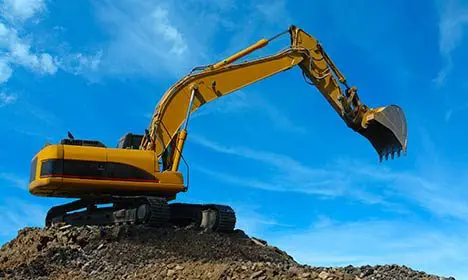 Yellow excavator on a mound of dirt against a blue sky with scattered clouds.