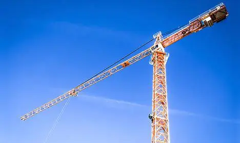 A tall construction crane with a lattice structure against a clear blue sky.