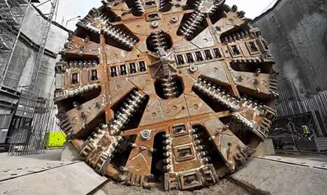 Close-up view of a large tunnel boring machine with metal cutting blades, positioned at a construction site.