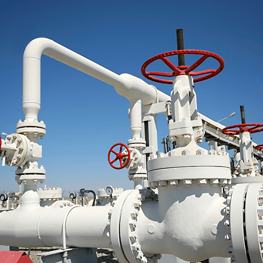 White industrial gas pipelines with red valve wheels under a clear blue sky.