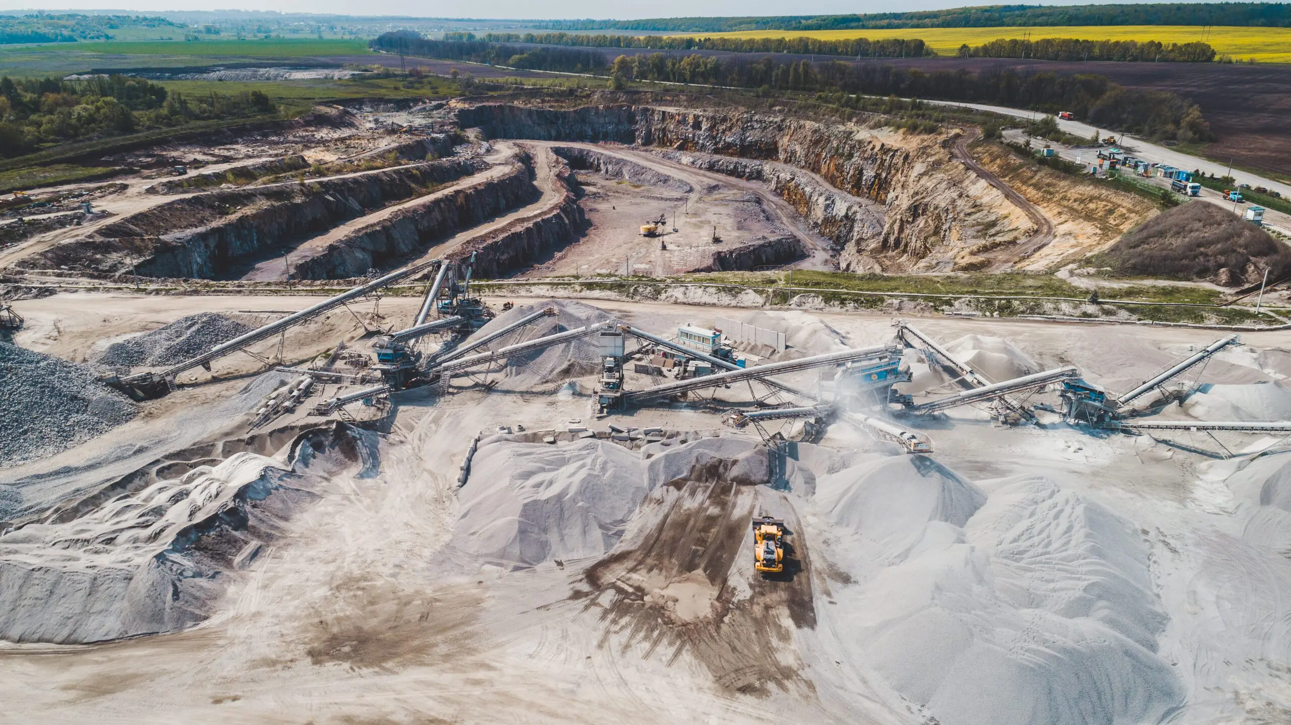 Aerial view of a large quarry with machinery and piles of gravel surrounded by fields and trees.
