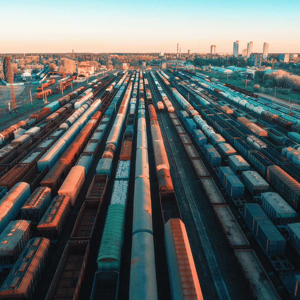 Aerial view of many freight train cars lined up on parallel tracks at a rail yard during sunset.