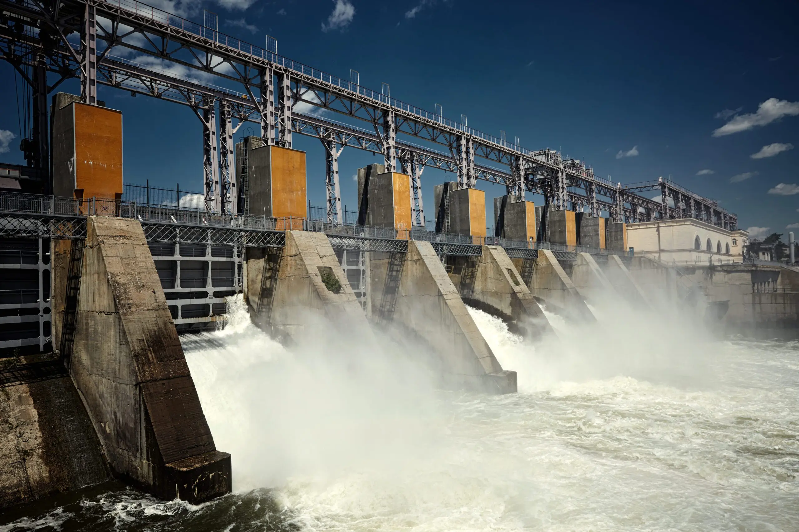 Water flows through the gates of a large hydroelectric dam under a clear, sunny sky.