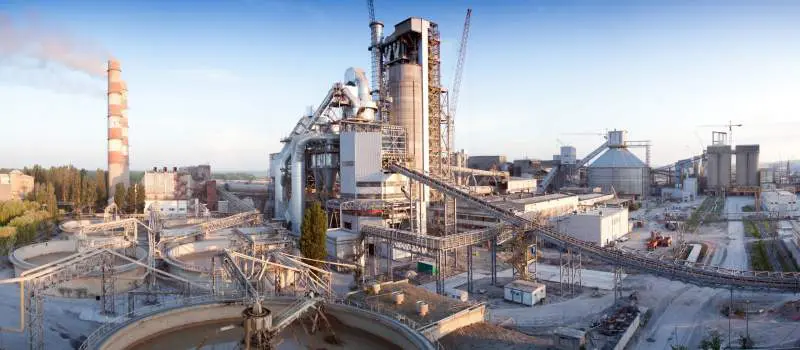 Wide view of an industrial complex with smokestacks, conveyors, and large storage silos under a clear sky.