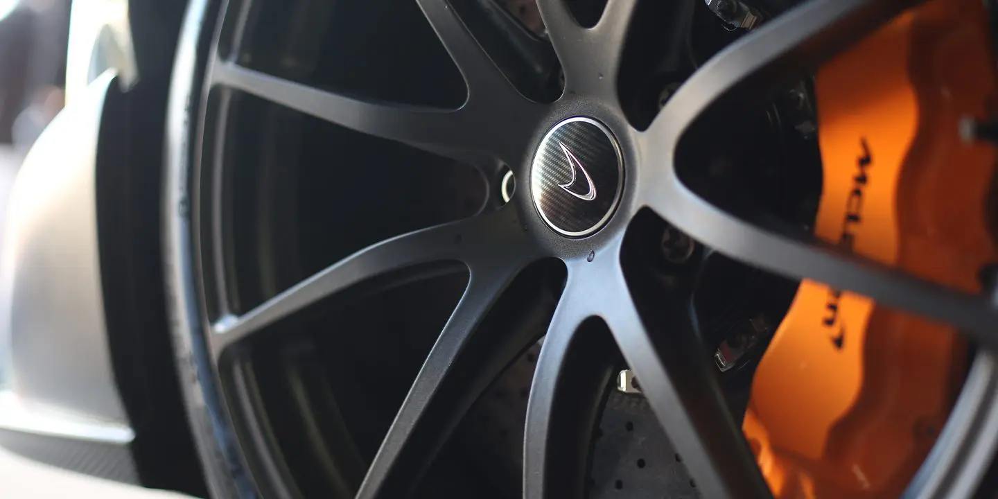Close-up of a black McLaren alloy wheel with an orange brake caliper behind it.