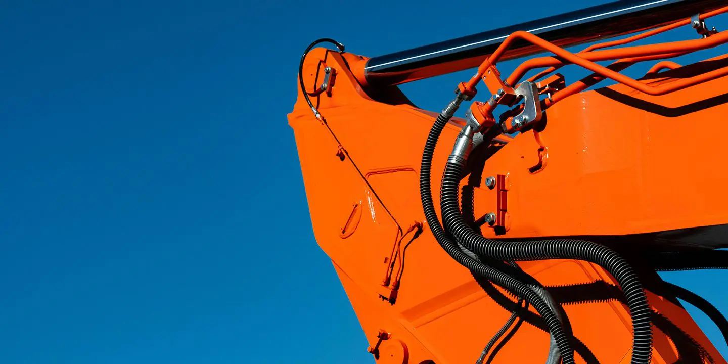 Close-up of an orange excavator arm with hydraulic hoses against a clear blue sky.