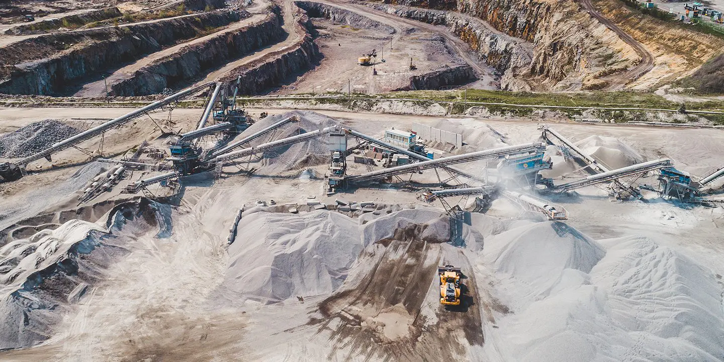 Aerial view of a large quarry with conveyor belts, sand piles, and heavy machinery at work.