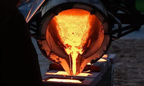 Molten metal being poured from a large crucible into molds at a foundry.