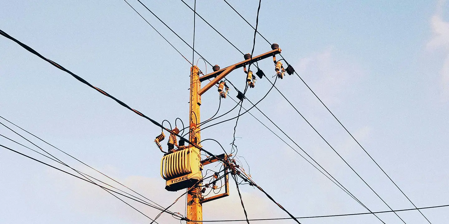 Wooden utility pole with multiple power lines and a transformer against a clear sky.