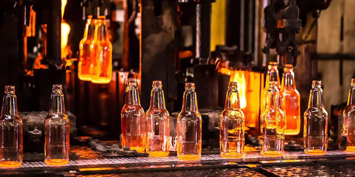 Rows of hot glass bottles being formed and cooled on an industrial production line in a factory.