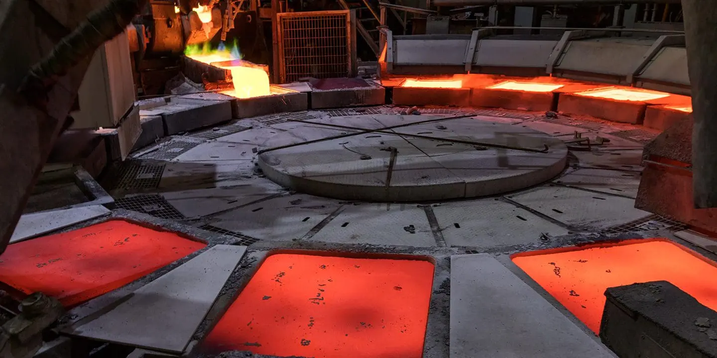 A circular industrial furnace with glowing red-hot tiles and molten metal being poured in the background.