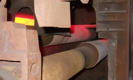 Hot steel slab being processed on rollers inside an industrial furnace, glowing bright orange.