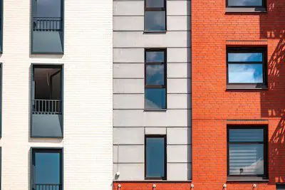 Modern building facade with white, gray, and red brick sections and several windows and balconies.
