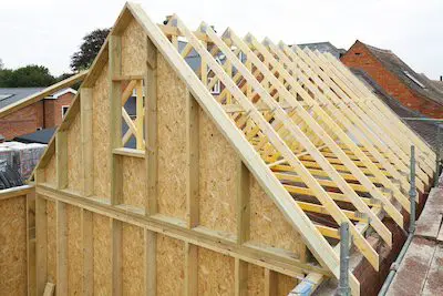 Wooden roof trusses being constructed on top of an unfinished house structure.