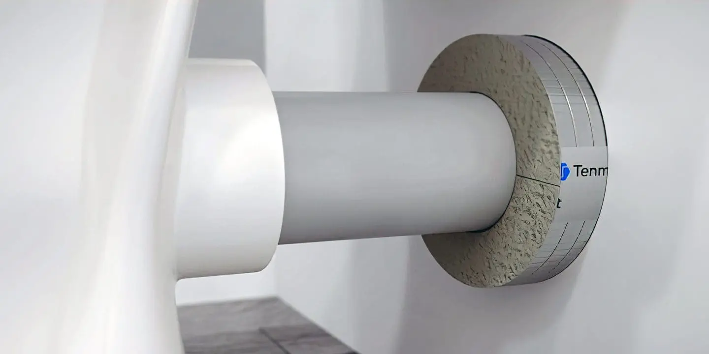 A large white pipe passes through a wall, sealed with a gray circular material for insulation or fire protection.