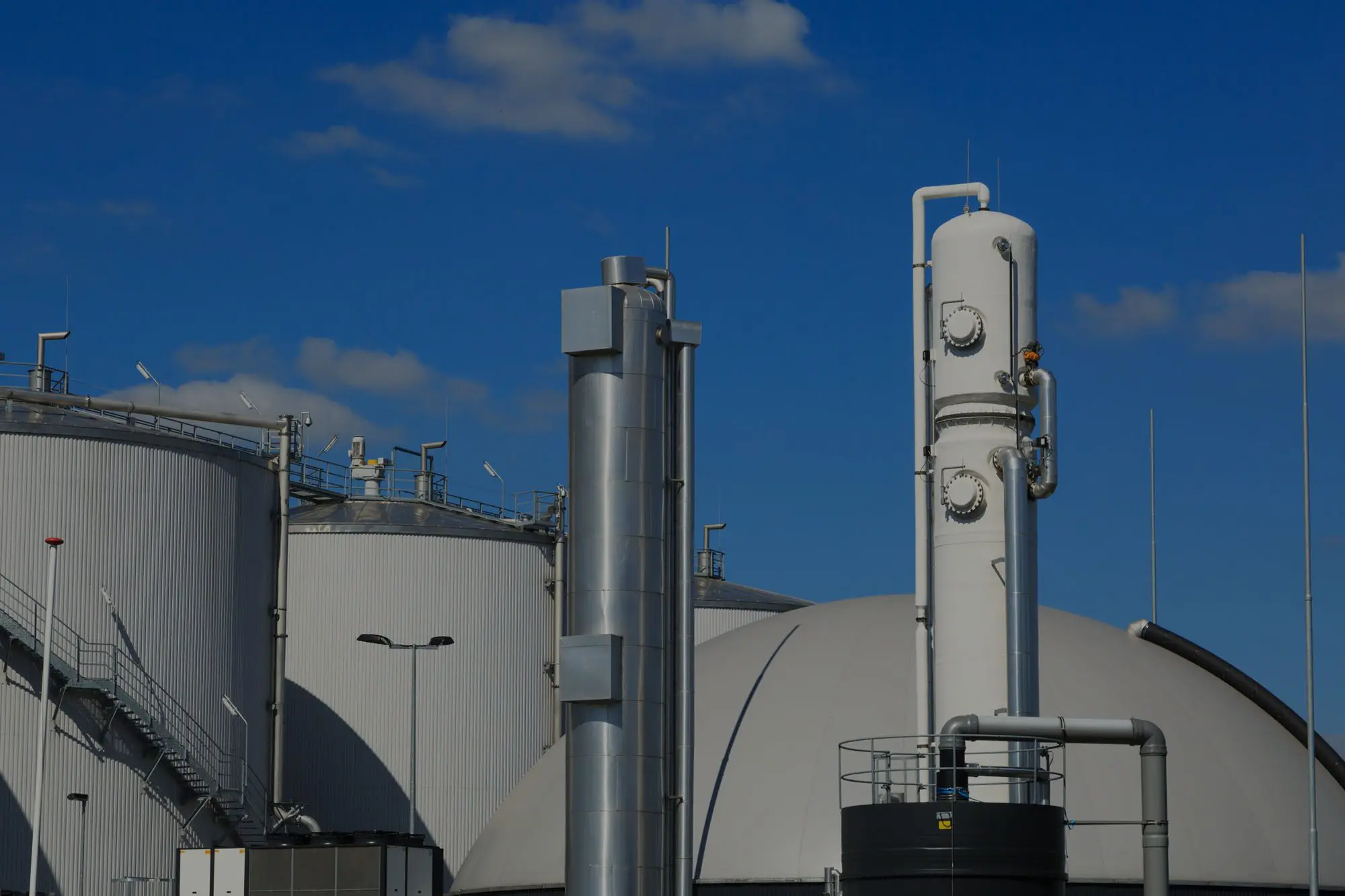 Industrial facility with large storage tanks and a worker on a tall white structure under a blue sky.