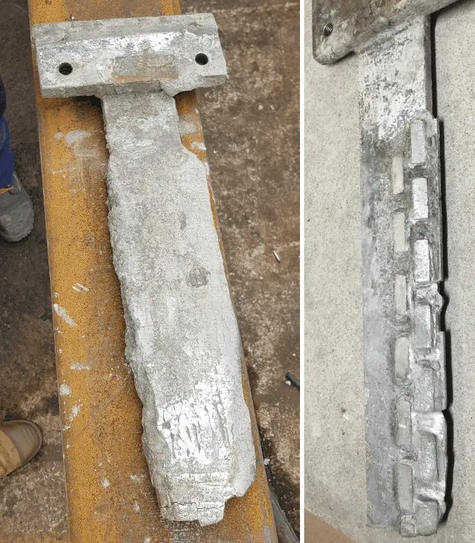 Two corroded metal objects with rough, uneven surfaces lie on a concrete and yellow metal background.