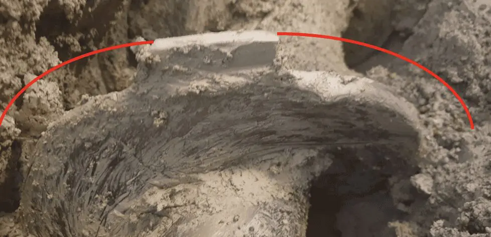 A muddy drilling tool with a red curved line indicating the buildup of clay on its surface.