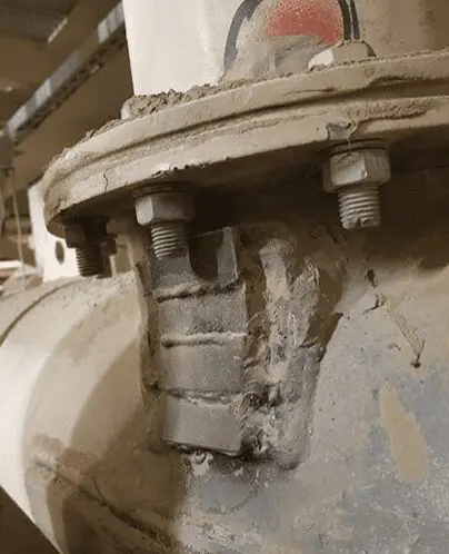 Close-up of a metal pipe with bolts and a cracked welded joint covered in dust.