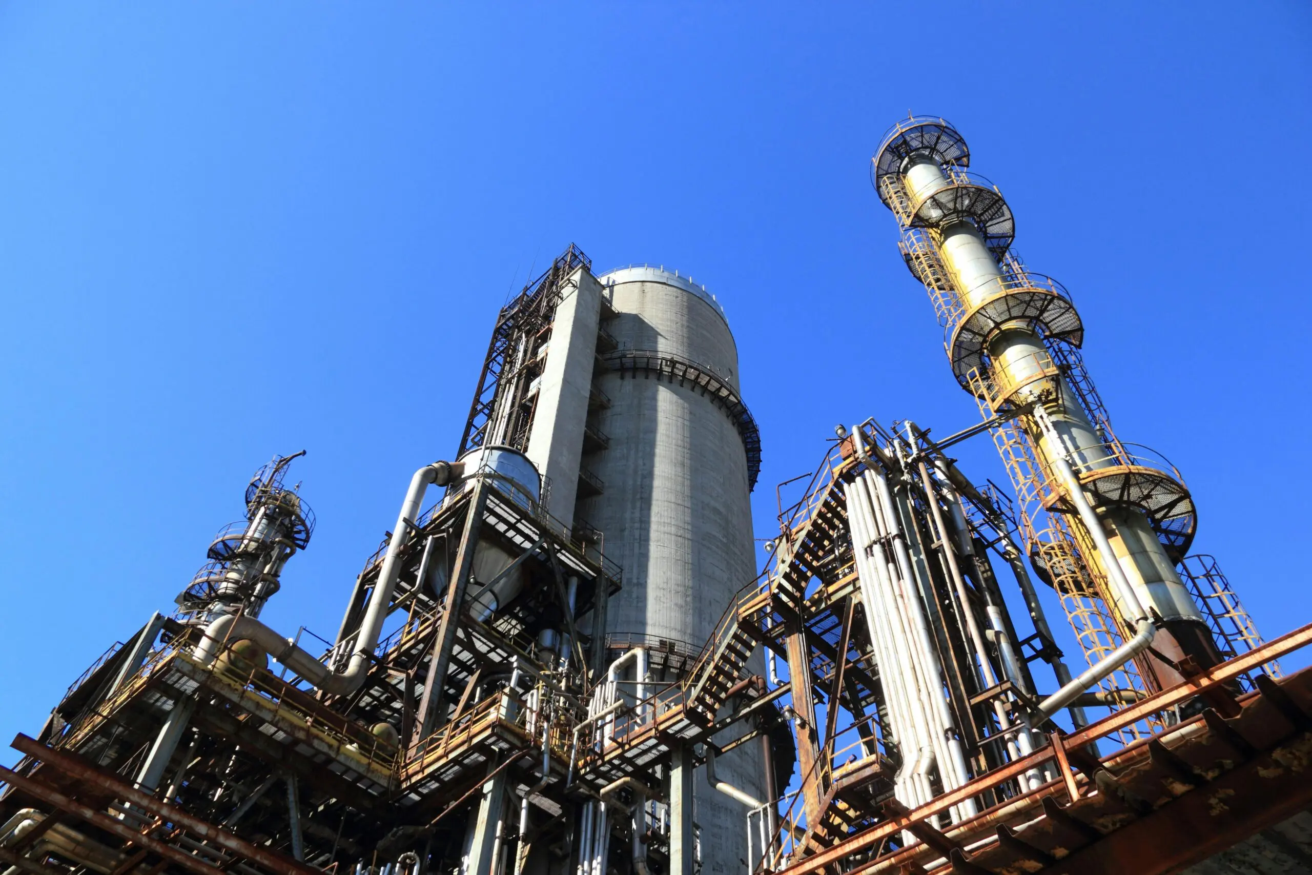 Industrial refinery towers and pipes with a clear blue sky in the background.