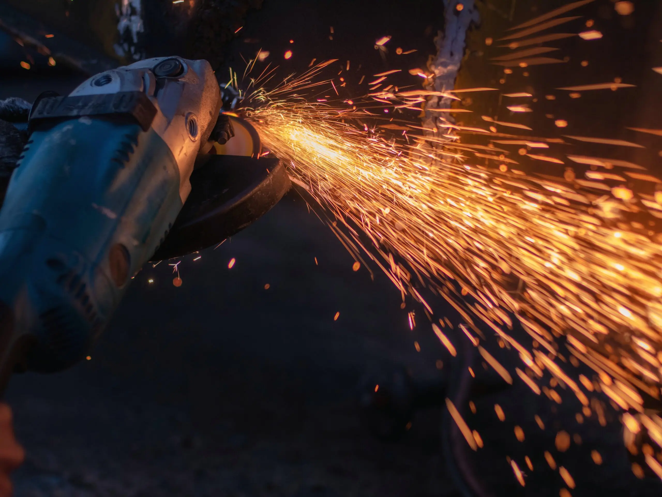 Close-up of an angle grinder cutting metal, with bright orange sparks flying outward.