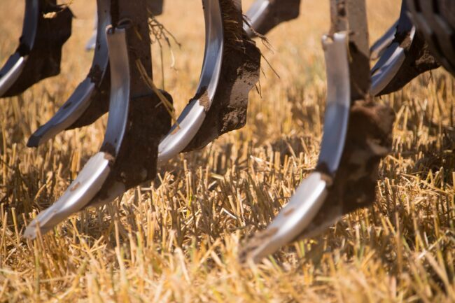 Nov 16 2020 Close-up of metal plow blades with soil on them, digging into a dry, harvested field.