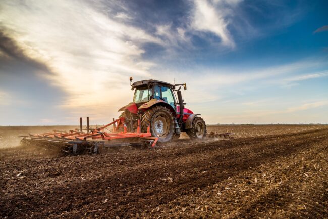 Feb 17 2021 A red tractor plowing a large field under a cloudy sky at sunset.