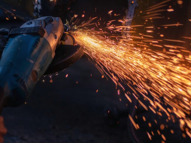 Worker,Grinding,Cutting,Metal,Sheet,With,Grinder,Machine,Overwrites,The A close-up of a grinder cutting metal, producing bright, flying sparks in the dark.