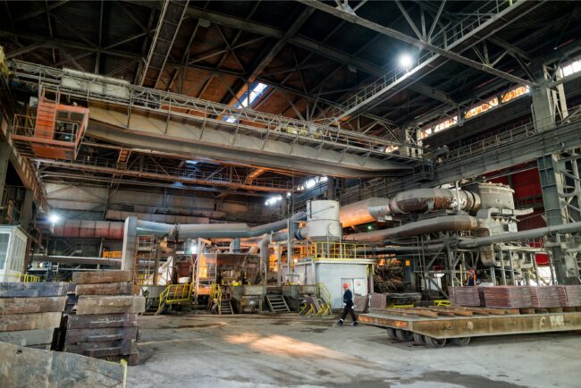 Mar 11 2021 Interior of a large industrial factory with machinery, metal platforms, and a worker walking on the floor.