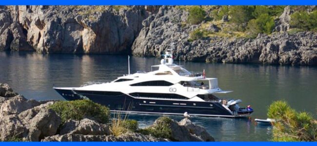 TENMAT-MONEY-SAVER Luxury yacht anchored in a calm bay surrounded by rocky cliffs and greenery.